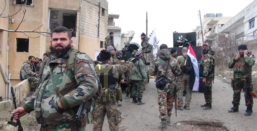 Forces loyal to the Syrian regime stand on a street with national flags after the Syrian army took control of the strategic town of Salma, in the  northwestern province of Latakia, on Tuesday (AFP photo)
